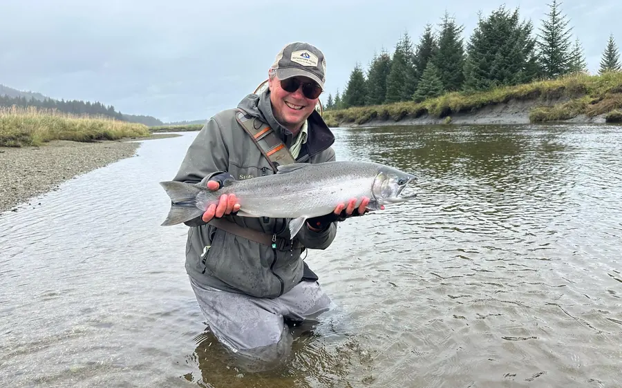 An angler standing in a shallow river holding a freshly caught Dolly Varden