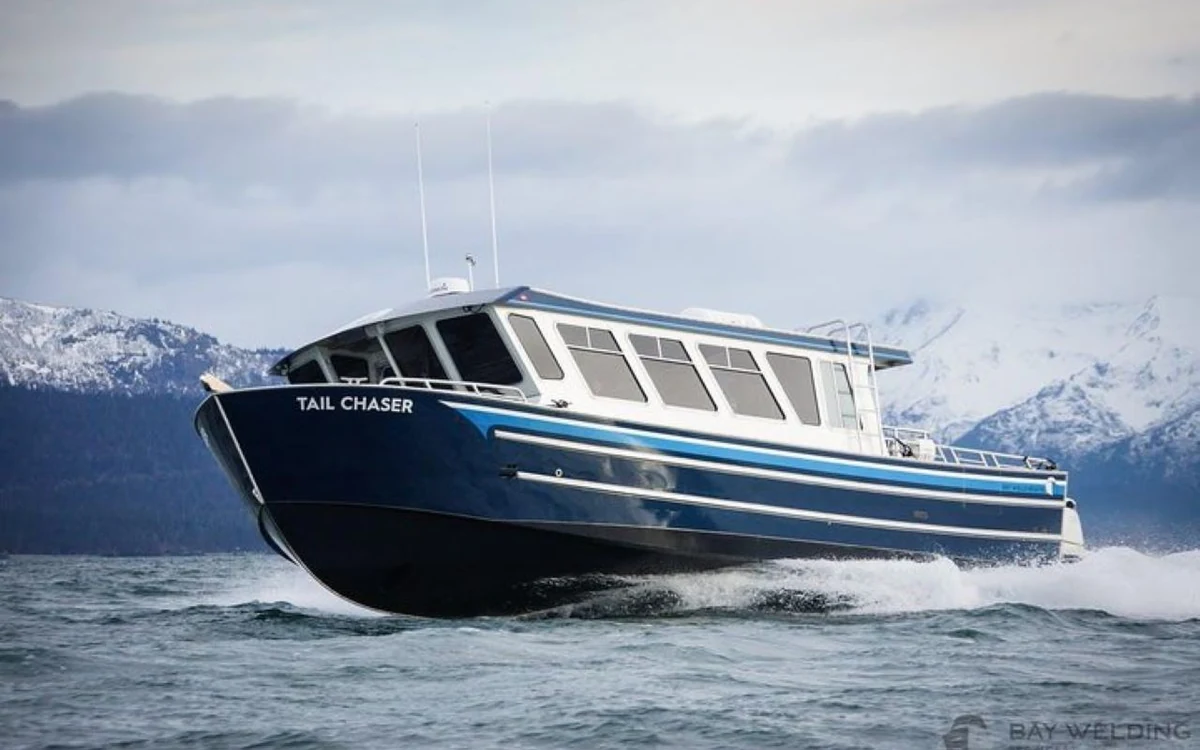 A small tour boat on the Icy Strait with snow-covered mountains behind